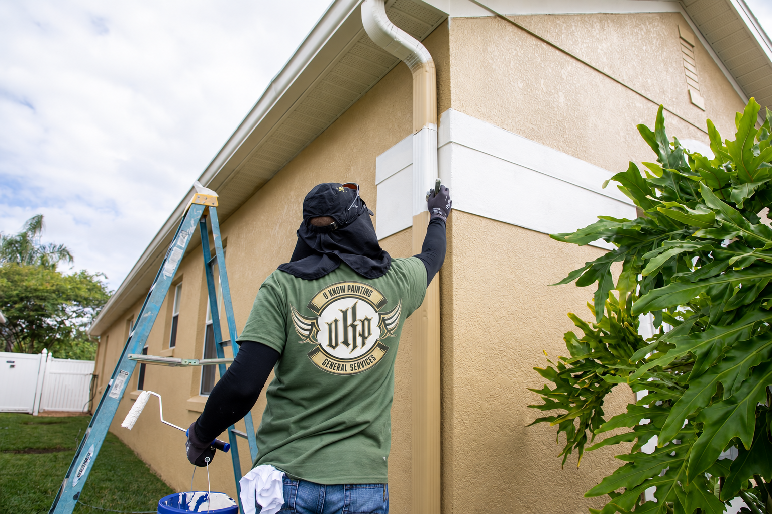 Anonymous professional painter carefully applying white exterior trim paint to a tan Central Florida home